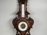 une horloge en bois accrochée au mur, sur laquelle est fixé un thermomètre