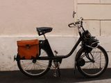a black bicycle parked next to a white wall with a brown bag on it