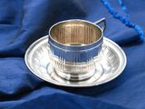 a silver cup and saucer sitting on a blue cloth