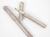 two silver pens sitting next to each other on top of a white surface