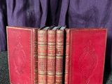 trois livres rouges posés sur une table, à côté d'un tissu violet