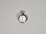 une petite montre de poche en or posée sur une surface blanche