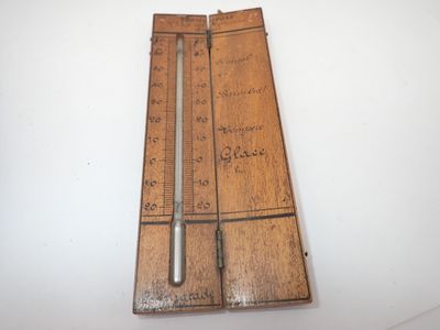 un vieux thermomètre en bois posé sur une table blanche, à côté d'une règle