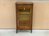 an old wooden cabinet with a glass door in front of a wall