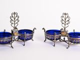 deux plats en verre argenté et bleu posés sur un support, sur une surface blanche