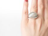 a woman ' s hand holding a silver ring with a shell on it