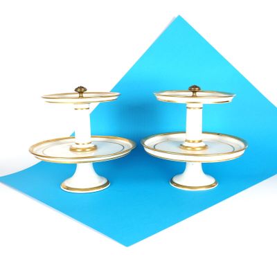 deux présentoirs à gâteaux blancs et dorés sur fond bleu