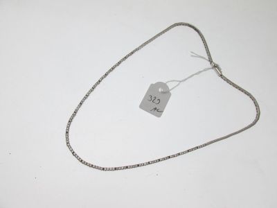 un collier en argent muni d'une plaque, posé sur une surface blanche