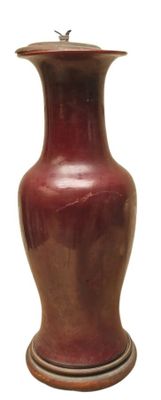 un vase rouge reposant sur un socle en bois, sur fond blanc