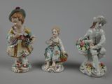 three porcelain figurines of a boy and a girl with baskets of flowers