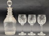 four wine glasses and a decanter sitting next to each other