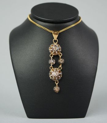 une image représentant un collier composé d'une chaîne en or et d'un pendentif en cristal