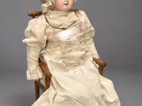 an antique doll sitting in a chair wearing a white dress and red shoes