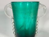 un vase en verre vert muni de deux anses, posé sur une surface blanche