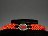 an orange beaded choke with a silver clasp on a black mannequin