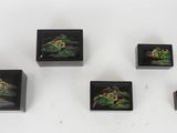 four small black boxes with paintings on them sitting on a white surface