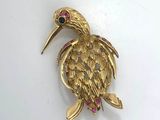 a close up of a gold bird brooch on a white surface