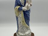 une figurine représentant une femme tenant un enfant dans ses bras, posée sur un socle en bois