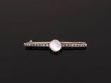 une broche en forme de barre, ornée d'une pierre de lune et de diamants, posée sur un fond noir