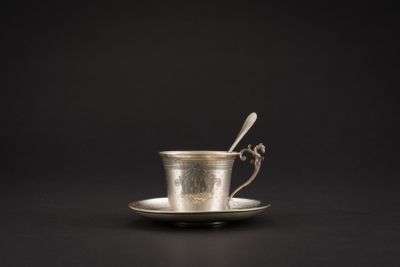une tasse en argent contenant une cuillère, posée sur une soucoupe