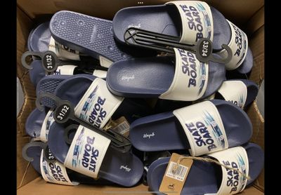 Plusieurs paires de sandales bleues et blanches sont empilées dans une boîte en carton