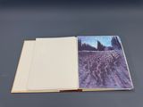 an open book sitting on top of a table with a painting on it
