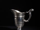 an antique silver pitcher on a black table with a black background