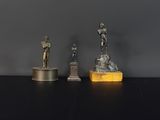 trois statues en bronze représentant un homme et une femme, posées sur un bloc de marbre