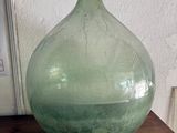un vase en verre vert posé sur une table près d'un mur blanc