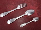 three silver spoons and a fork on a red cloth
