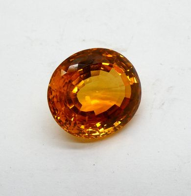 un saphir orange posé sur une surface blanche, avec un fond blanc