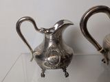 two silver pitchers sitting on a glass table