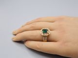 a woman ' s hand holding a ring with a green stone on it