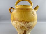 a yellow vase with handles sitting on a white surface