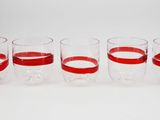 six verres aux bords rouges sont alignés sur une surface blanche