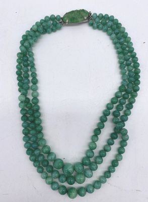un gros plan d'un collier de perles vertes posé sur une surface blanche