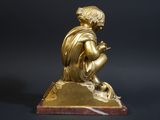 gold statue of a boy sitting on a rock with a bird in his hand