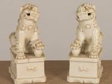 pair of white ceramic foo foo statues sitting on top of a wooden table