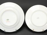 two white plates with a green design on them on a black surface