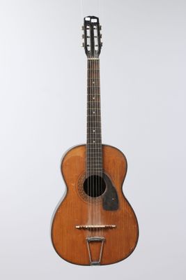 an old wooden guitar hanging from a string on a white wall