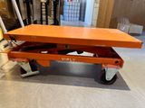 a orange lift table with wheels on it in a warehouse