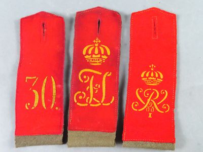 trois insignes rouges ornés de lettres dorées et d'une couronne