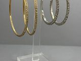 trois paires de boucles d'oreilles créoles en or et en argent, présentées sur un présentoir en acrylique transparent