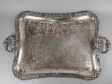 an ornate silver tray with handles on a white surface