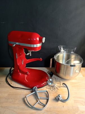 un batteur rouge posé sur une table en bois, à côté d'un saladier
