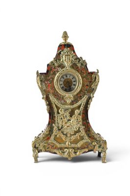 a gold and red clock on a stand on a white surface