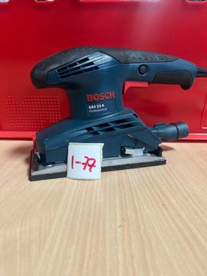 une ponceuse orbitale Bosch posée sur une table, à côté d'une boîte rouge
