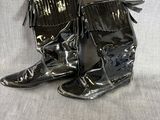 une paire de bottes en cuir noir ornées de franges, posées sur une surface blanche