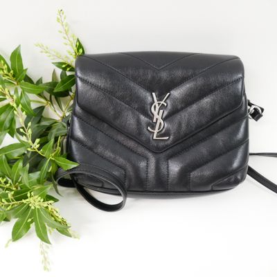 a black saint laurent bag next to a plant on a white surface