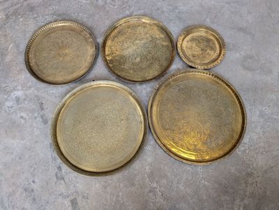 six plateaux en laiton avec leurs couvercles sont posés sur une surface en ciment
